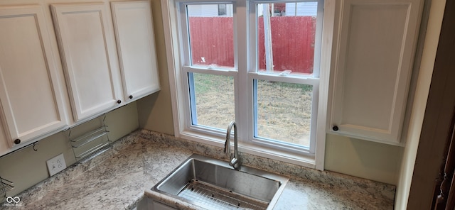 kitchen with white cabinets, light stone countertops, sink, and a wealth of natural light