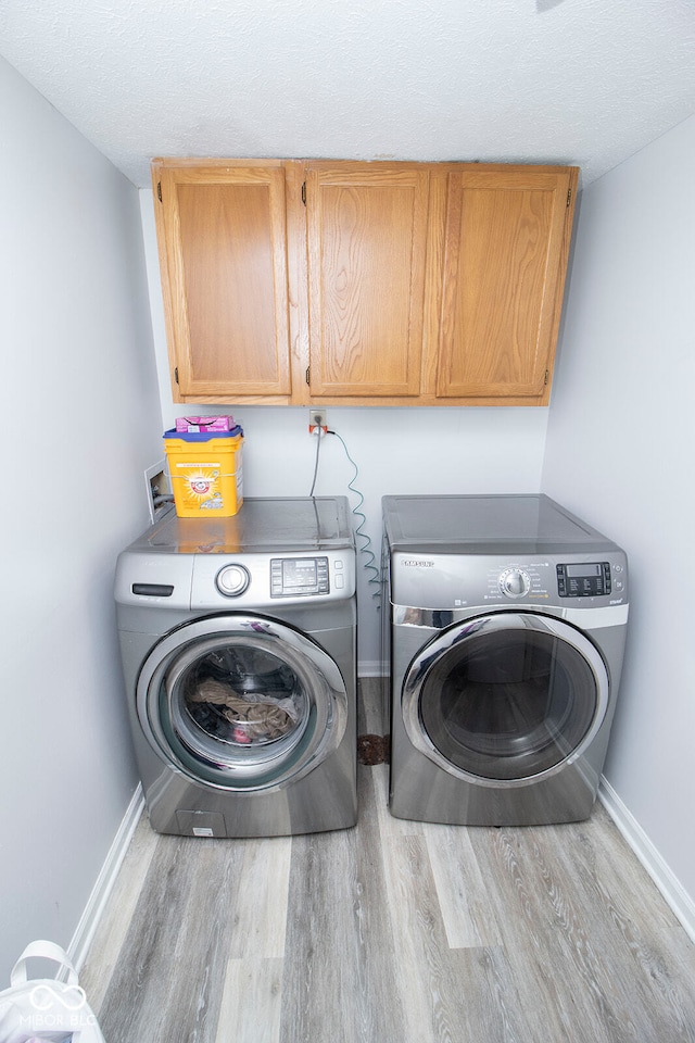 laundry area with light wood-type flooring, cabinets, a textured ceiling, and separate washer and dryer