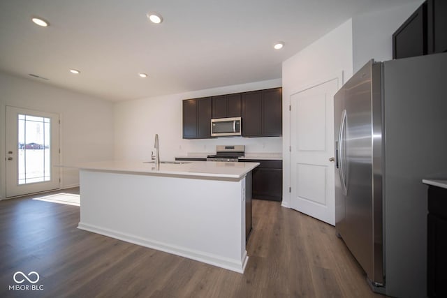 kitchen featuring dark brown cabinetry, appliances with stainless steel finishes, dark wood-type flooring, sink, and a kitchen island with sink