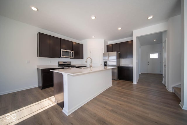 kitchen with stainless steel appliances, dark hardwood / wood-style floors, a kitchen island with sink, dark brown cabinets, and sink