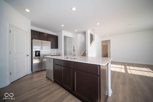 kitchen with dark brown cabinetry, appliances with stainless steel finishes, an island with sink, sink, and light hardwood / wood-style flooring