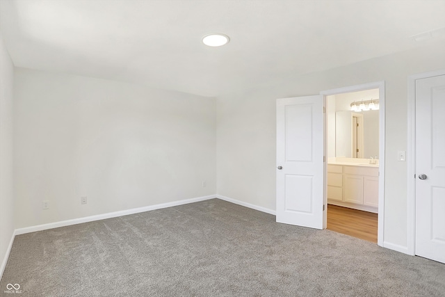 unfurnished bedroom featuring sink, ensuite bathroom, and carpet flooring