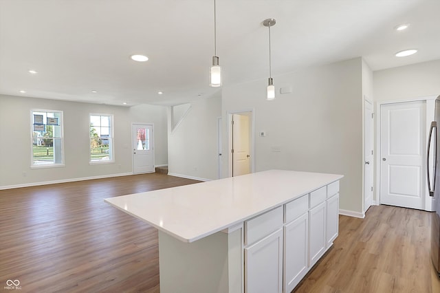 kitchen featuring a kitchen island, white cabinetry, stainless steel refrigerator, light hardwood / wood-style flooring, and decorative light fixtures