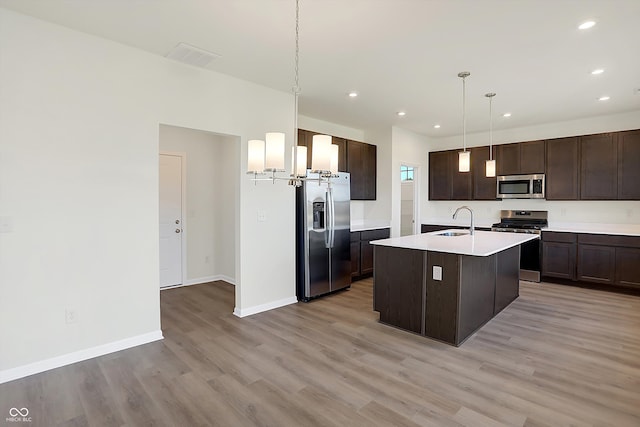 kitchen featuring an island with sink, sink, pendant lighting, light wood-type flooring, and appliances with stainless steel finishes