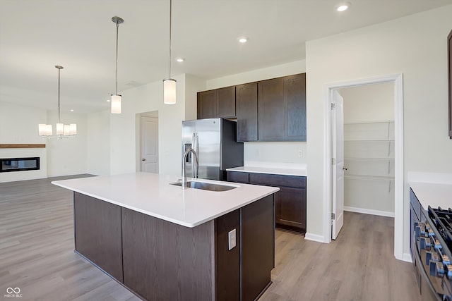 kitchen with stainless steel appliances, a center island with sink, sink, dark brown cabinetry, and light wood-type flooring