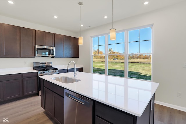 kitchen featuring a kitchen island with sink, light hardwood / wood-style flooring, sink, pendant lighting, and stainless steel appliances