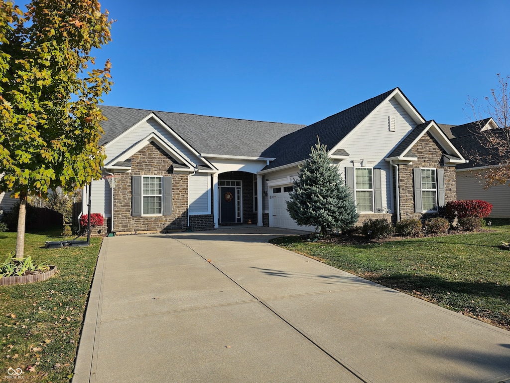 view of front of home with an attached garage, driveway, stone siding, and a front yard