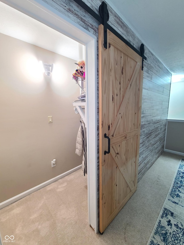 hall with light carpet, a barn door, and wooden walls