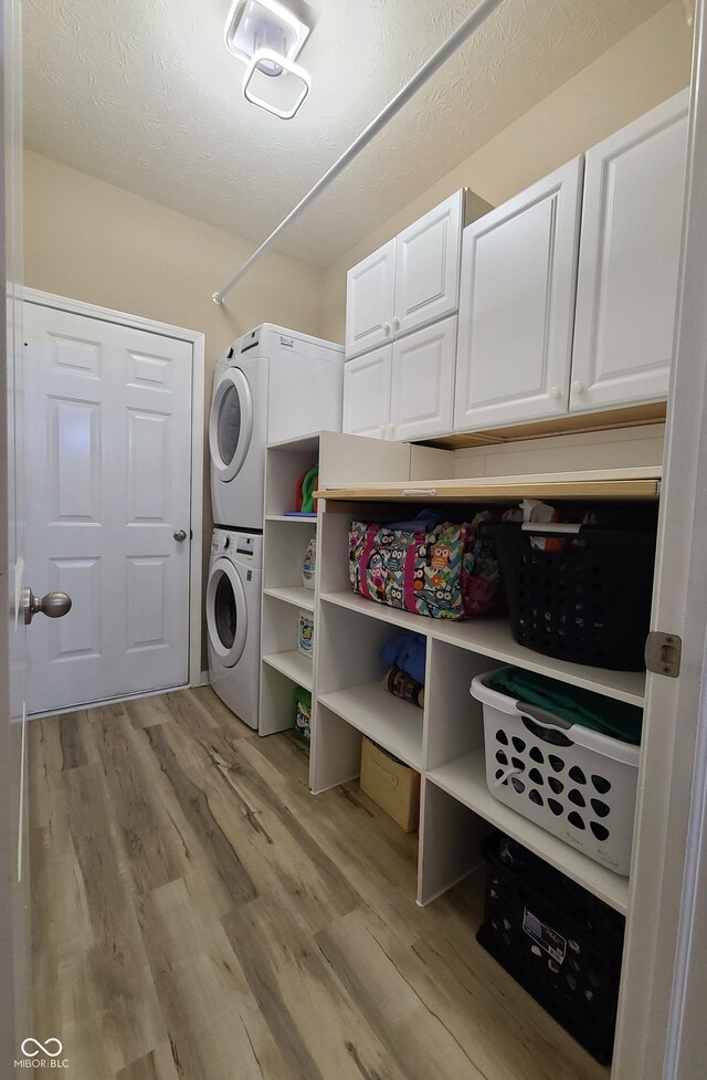 washroom featuring stacked washer / dryer, cabinets, and light hardwood / wood-style floors