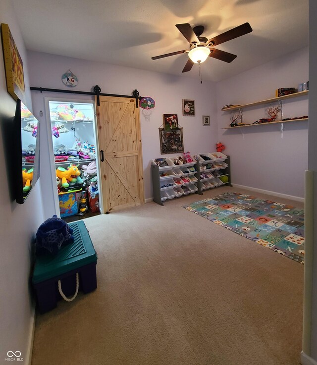 rec room with carpet flooring, ceiling fan, and a barn door