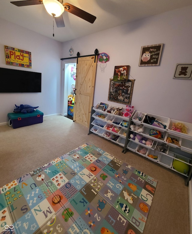 recreation room with carpet, a barn door, and ceiling fan