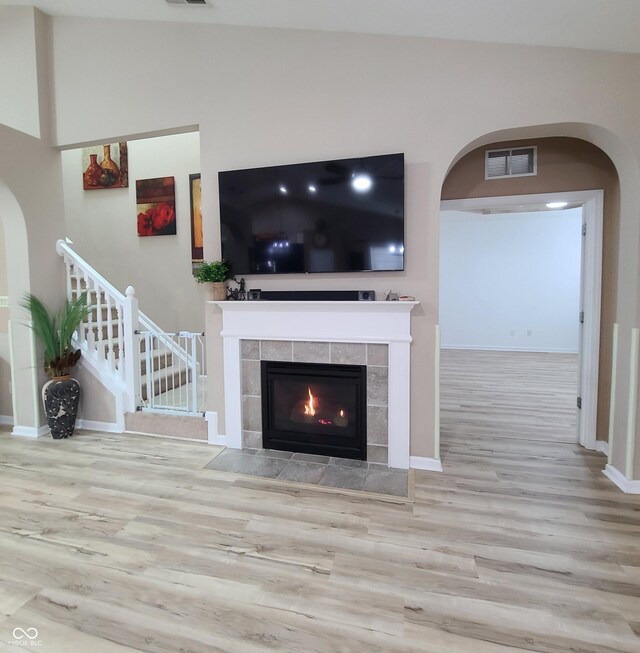 living room featuring a tile fireplace, light hardwood / wood-style flooring, and vaulted ceiling