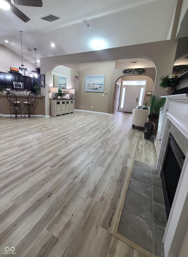 living room with a tiled fireplace, ceiling fan, lofted ceiling, and light wood-type flooring