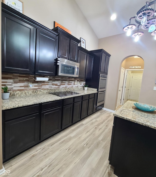 kitchen featuring decorative backsplash, light stone counters, stainless steel appliances, and light hardwood / wood-style flooring