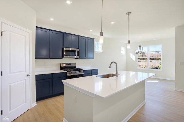 kitchen featuring appliances with stainless steel finishes, sink, an island with sink, pendant lighting, and light hardwood / wood-style flooring