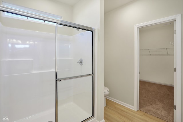 bathroom featuring toilet, a shower with shower door, and wood-type flooring