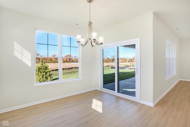 unfurnished dining area featuring a wealth of natural light, a notable chandelier, and light wood-type flooring