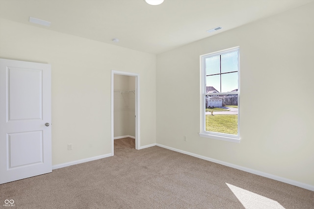 unfurnished bedroom with a closet, light carpet, and a walk in closet