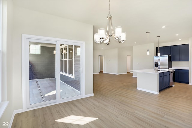 kitchen featuring a kitchen island with sink, stainless steel fridge, a notable chandelier, pendant lighting, and light wood-type flooring