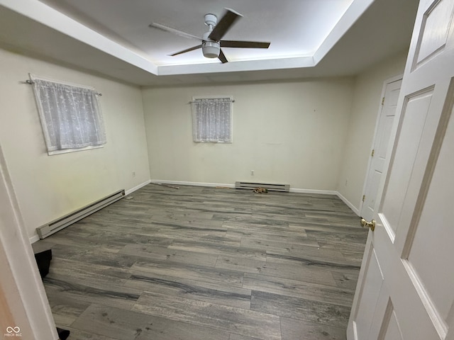 empty room featuring baseboard heating, dark wood-type flooring, ceiling fan, and a raised ceiling