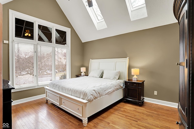 bedroom featuring vaulted ceiling with skylight, baseboards, and wood finished floors