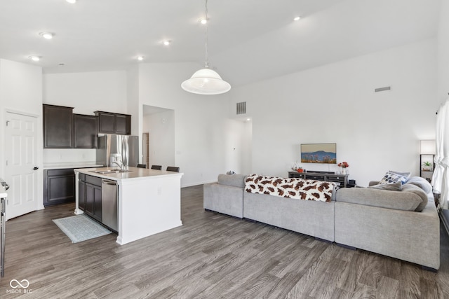 kitchen with a kitchen island with sink, dark brown cabinetry, wood-type flooring, and high vaulted ceiling