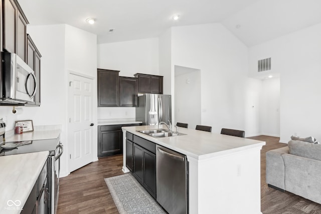 kitchen featuring dark hardwood / wood-style floors, an island with sink, sink, appliances with stainless steel finishes, and high vaulted ceiling