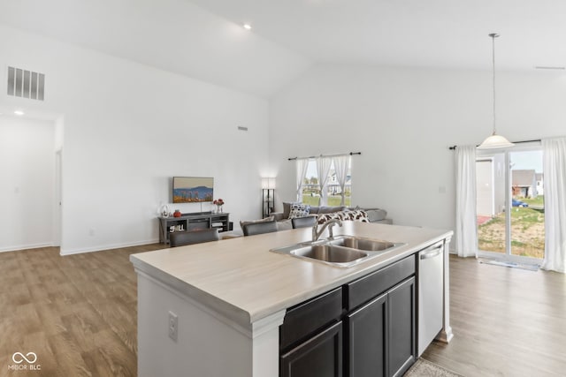 kitchen with sink, light hardwood / wood-style floors, decorative light fixtures, high vaulted ceiling, and a kitchen island with sink