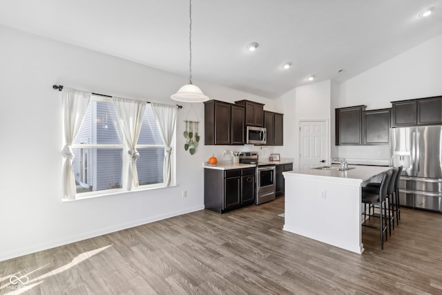 kitchen featuring an island with sink, hanging light fixtures, wood-type flooring, vaulted ceiling, and appliances with stainless steel finishes