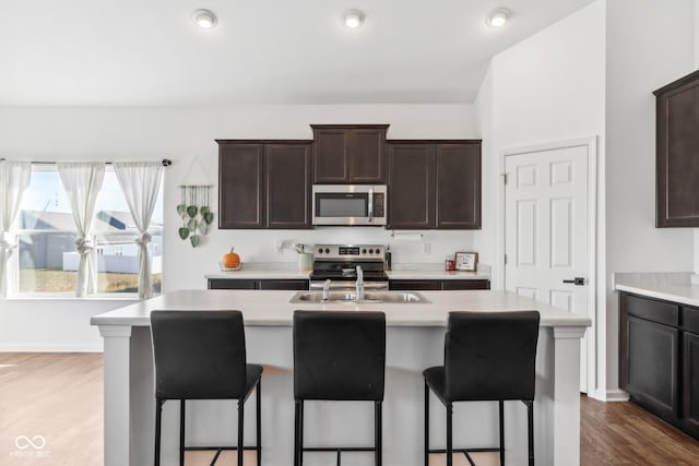 kitchen with a breakfast bar, stainless steel appliances, wood-type flooring, and an island with sink