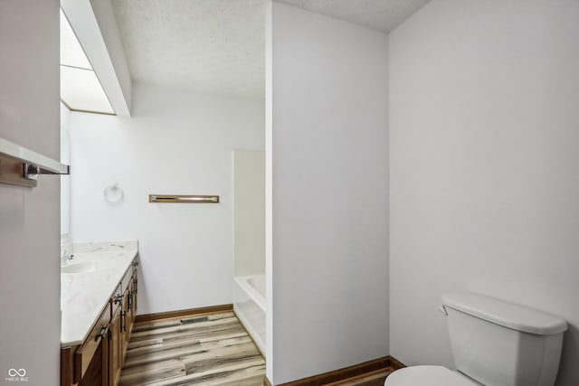 bathroom featuring a tub, a textured ceiling, toilet, vanity, and hardwood / wood-style flooring