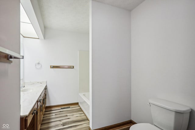 full bathroom with vanity, wood finished floors, toilet, a bathtub, and a textured ceiling