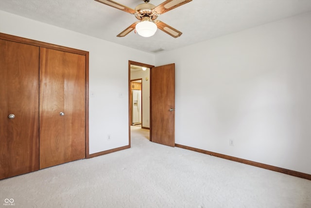 unfurnished bedroom featuring white refrigerator with ice dispenser, light colored carpet, a closet, and ceiling fan