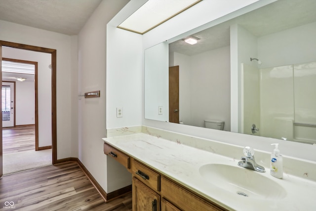 bathroom with hardwood / wood-style floors, a textured ceiling, walk in shower, toilet, and vanity