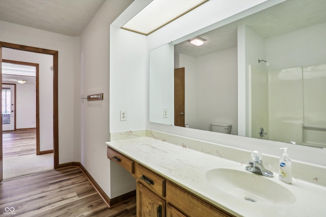 full bath with wood finished floors, toilet, a shower, baseboards, and vanity