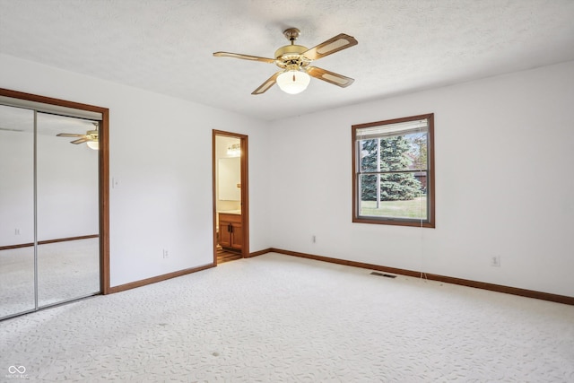unfurnished bedroom with baseboards, light colored carpet, a closet, connected bathroom, and a textured ceiling