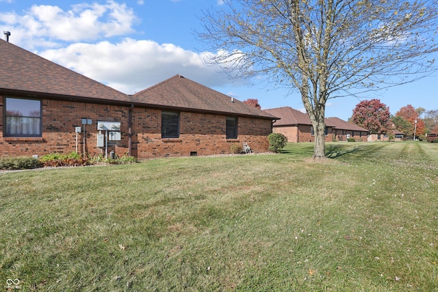 view of home's exterior with brick siding, a lawn, and roof with shingles