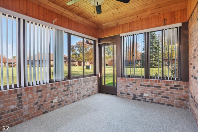 unfurnished sunroom featuring brick wall, a ceiling fan, carpet, and wood ceiling