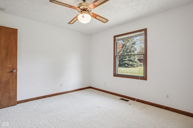 spare room with ceiling fan, baseboards, light colored carpet, and a textured ceiling