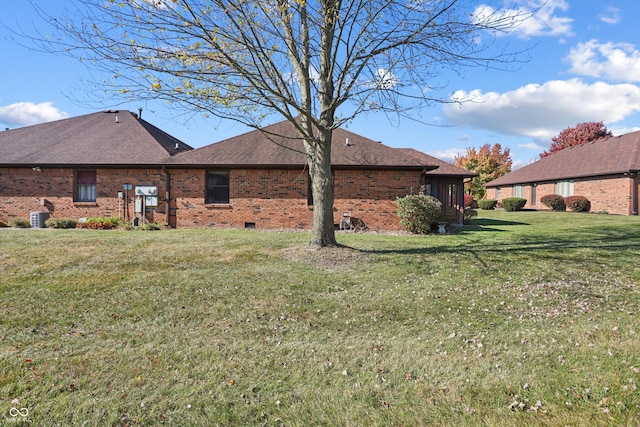 back of house with brick siding, central AC unit, a yard, and roof with shingles