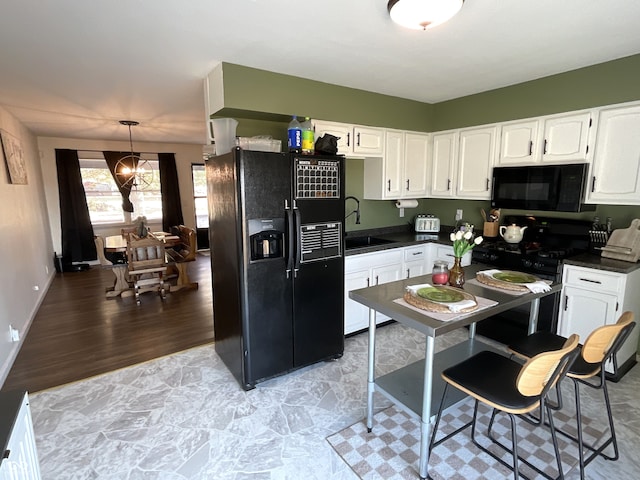 kitchen with white cabinets, hanging light fixtures, light hardwood / wood-style flooring, black appliances, and sink