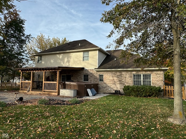 rear view of house featuring a hot tub and a lawn