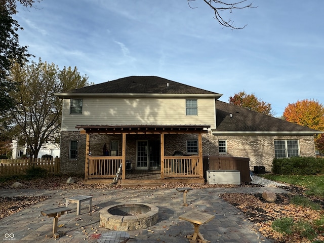 back of property featuring a hot tub, a deck, a patio area, and an outdoor fire pit