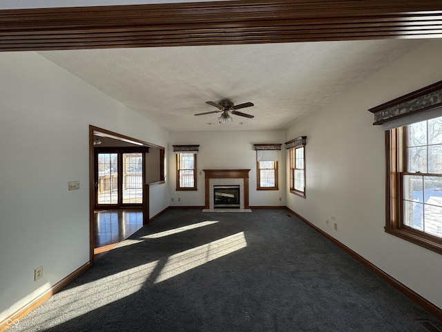 unfurnished living room featuring ceiling fan, a tiled fireplace, a textured ceiling, and dark colored carpet