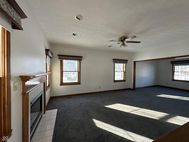 unfurnished living room with plenty of natural light, a tiled fireplace, dark carpet, and a textured ceiling