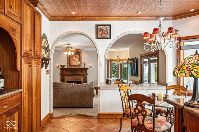 6902 Creekridge Trl, Indianapolis, IN 46256 - dining space with a chandelier, ornamental molding, tile patterned floors, a lit fireplace, and a ceiling fan