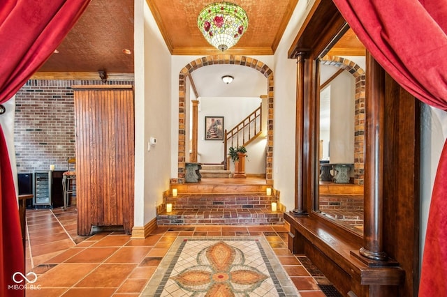 hallway with tile patterned flooring, beverage cooler, brick wall, and ornamental molding