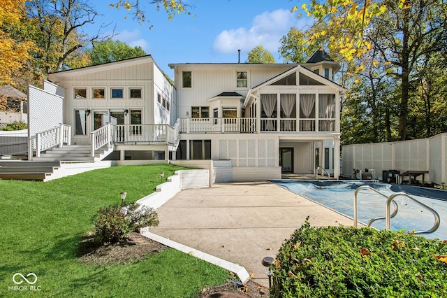 back of property with a sunroom, a pool side deck, a patio, and a lawn