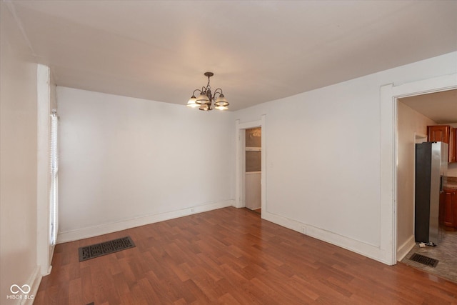 unfurnished room featuring visible vents, baseboards, wood finished floors, and a chandelier