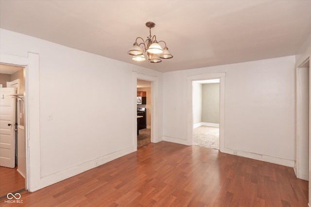 spare room with wood finished floors, baseboards, and a chandelier